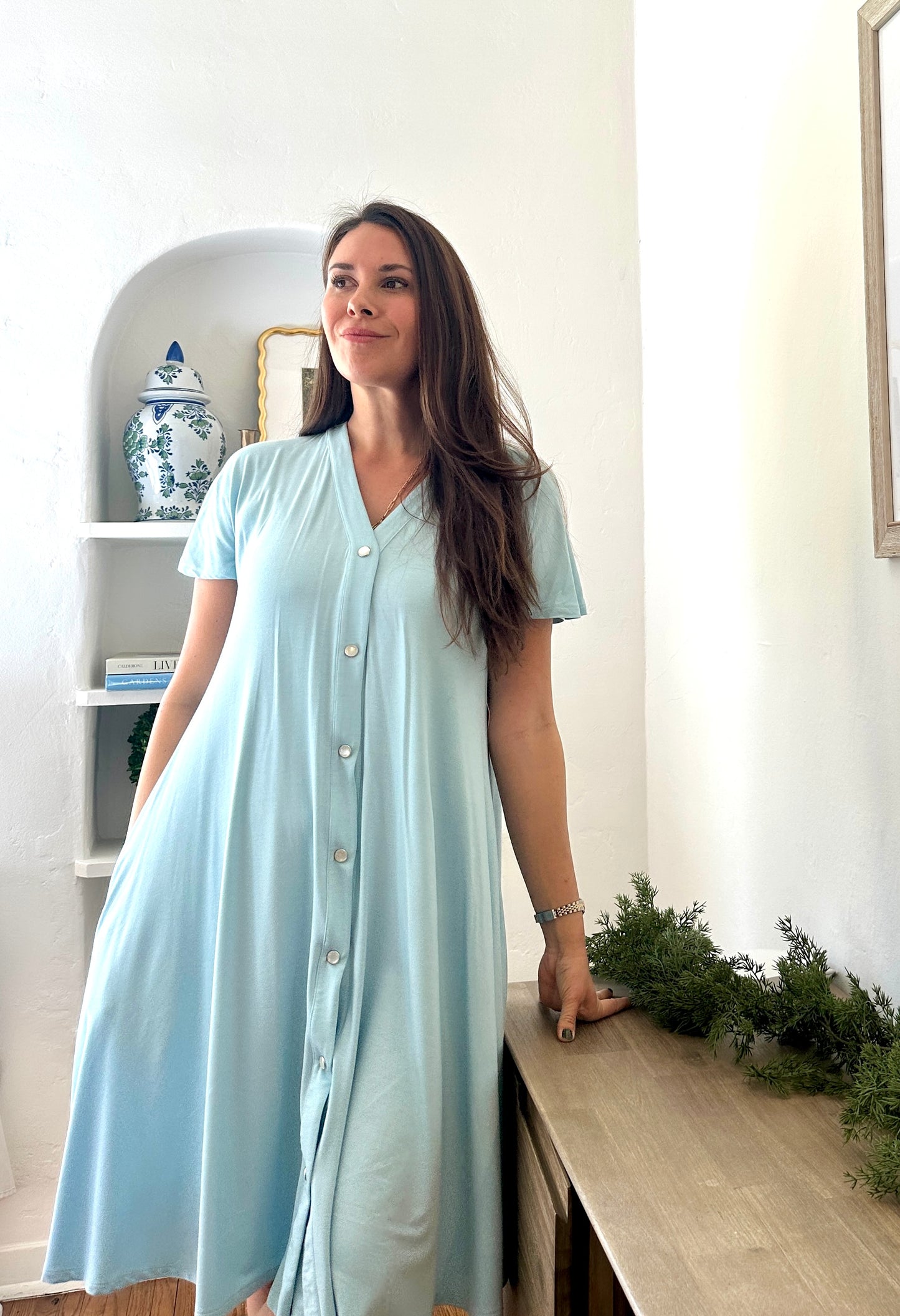 A woman wearing a blue postpartum gown with snap buttons down the front.