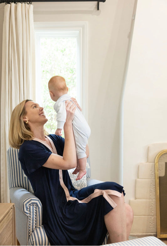 Woman holding a baby in a room with white curtains and furniture.