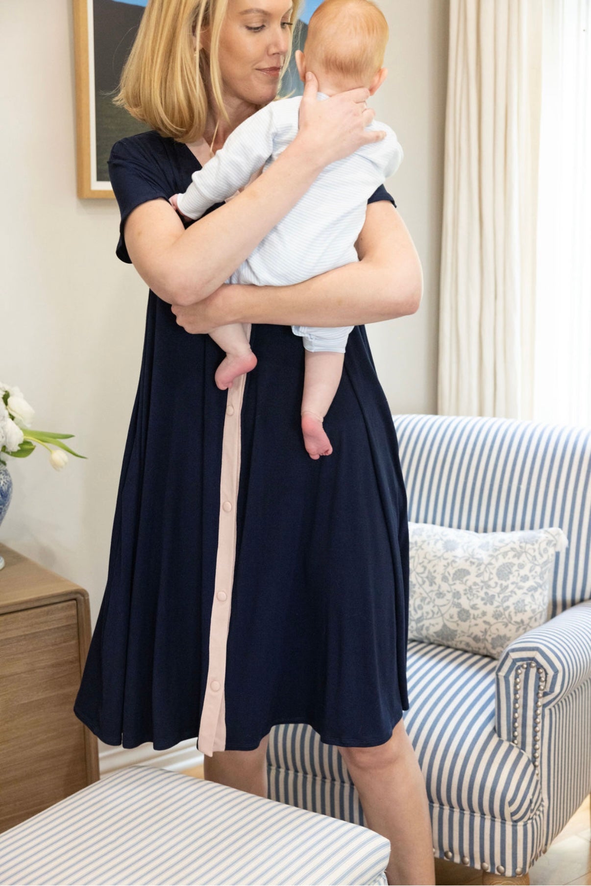 Woman in a navy dress holding a baby in a living room.
